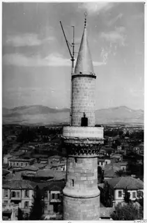Tall stone tower with a conical cap and crescent finial rising above the roofs of Nicosia, with mountains behind