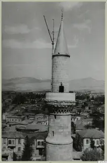 Tall stone tower with a conical cap rising above the rooftops of Nicosia, with mountains beyond.