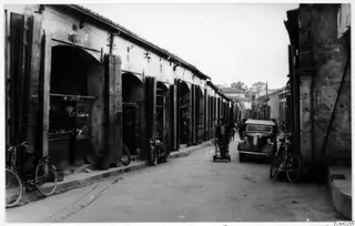 Street in Nicosia lined with arched shop fronts, with a parked car, bicycles and a motorcycle