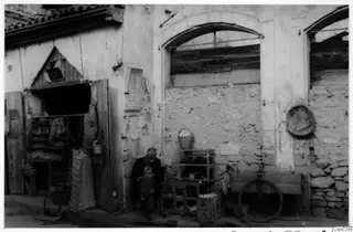 Man seated in a Nicosia street beside a plastered wall, wooden crates and a wooden cart