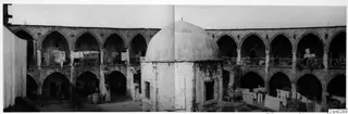 Courtyard of a two-storey arcaded building in Nicosia, with washing hung on lines and a large barrel on the ground.