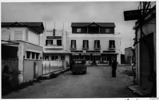 Street in Famagusta with a parked car, white two-storey buildings and a standing man