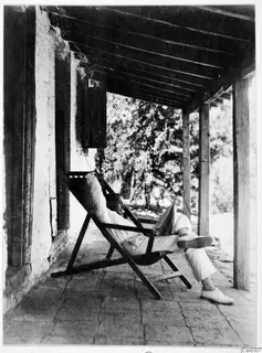 Erik Sjöqvist (?) reading a newspaper in a canvas deck chair on a veranda