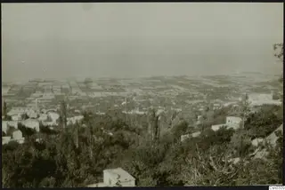 Elevated view over a town of white houses, cultivated fields and trees, with hazy sea beyond