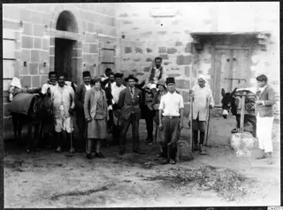 Group of people and two donkeys in a courtyard in front of a stone building with an arched doorway