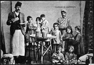 Posed group of ten people, with children around a small round table holding a tall bottle and a metal canister.