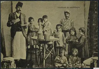 Posed studio group of two men and several children around a small round table with a glass bottle and a tin cup.