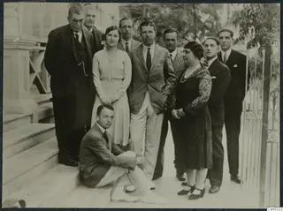 Group of ten people posed on the front steps of the Pierides house in Larnaca, beside an iron gate.