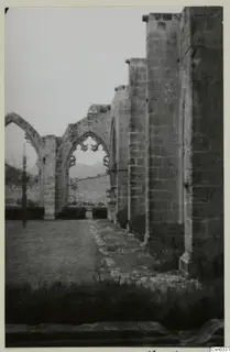 Ruined monastery walls with pointed arches and a paved path beside a grassy courtyard