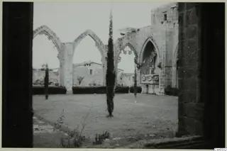 Ruined monastery at Bellapais with pointed arches and tall cypress trees around a grassy courtyard