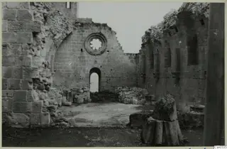 Monastery ruin: stone walls with a round window and arched doorway, with rubble and column drums on the ground