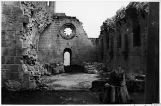 Ruined monastery interior with a round window and an arched doorway with bars, set in stone walls