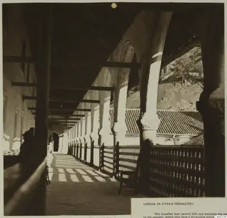 Covered loggia with columns and arches in Kykko Monastery, with a tiled roof and rocky hillside beyond.