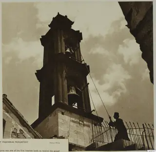 Belfry at Makheras Monastery seen from below, with a man pulling a rope to ring the bells.