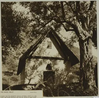 Small building with a steep pitched roof and pale gable wall beneath a large tree, Solea Valley