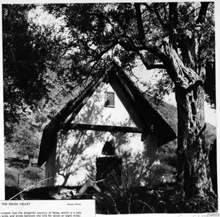 Small whitewashed building with a pitched roof and one window, under a large tree in the Solea Valley
