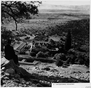 St Chrysostomos Monastery seen from a rocky hillside, with a seated man in the foreground looking over the valley