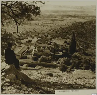 St Chrysostomos Monastery seen from a rocky hillside, with a seated man in the foreground