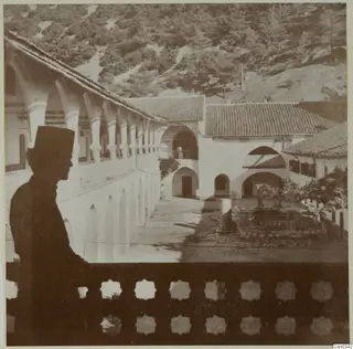 Kykko Monastery: arcaded courtyard range seen past a silhouetted man leaning on a balcony railing.