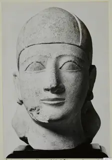 Limestone head of a statue with a close-fitting cap, shown frontally on a dark wooden base