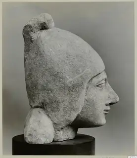 Limestone head of a figure in profile, wearing a tall headdress, shown on a dark cylindrical stand.