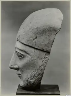 Limestone Neo-Cypriote head of a bearded figure in side view, wearing a tall headdress, on a dark stand