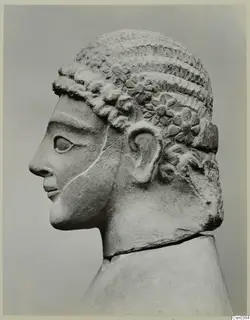 Limestone statue head in profile, facing left, with tiered curled hair and rosette ornaments above the ear.
