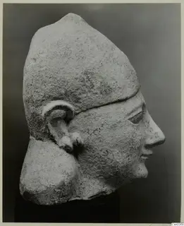 Limestone head in profile wearing a tall cap-like headdress, with a rough, weathered surface