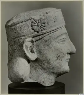 Limestone Neo-Cypriote head in right profile, with a rosette on its headband, on a dark cylindrical stand