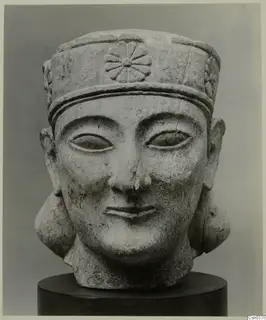Limestone Neo-Cypriote head sculpture with a tall cylindrical headdress, shown on a dark stand