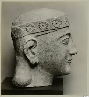 Limestone head of a figure in three-quarter profile, wearing a band with rosette ornament around the forehead.
