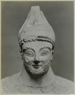 Limestone statue head and shoulders of a bearded figure wearing a tall conical headdress, shown from the front.