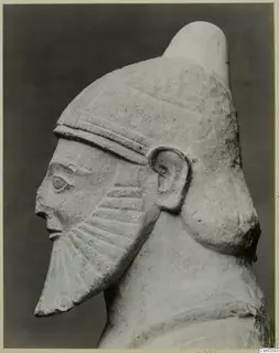 Limestone sculpture of a bearded head in side profile, wearing a tall cylindrical cap