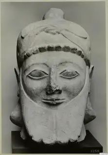 Carved limestone head of a bearded figure with a bead band and a hair knot