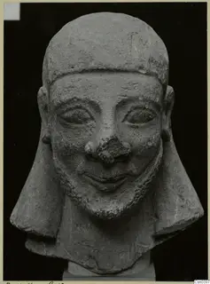 Limestone head sculpture with a smiling face and short beard, shown from the front.