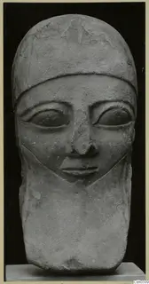 Carved limestone head sculpture with a close-fitting cap, large eyes and a straight nose, shown against a black background.