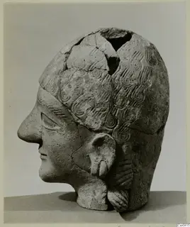Terracotta head in profile facing left, with incised wavy hair and the top of the skull broken open.