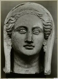 Limestone head of a female figure with wavy hair and a tall veil, photographed frontally against a dark backdrop