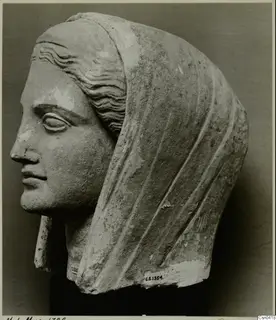 Limestone head with a veil drawn over the back, shown in left profile, with the face and surface partly worn.