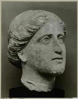 Limestone head of a woman with wavy hair combed back from the face.