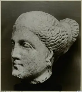 Limestone head of a statue with wavy hair drawn back into a large bun at the back