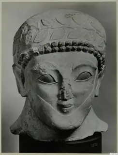 Limestone head of a figure with a laurel-like band of leaves and rows of curls over the forehead, photographed against a grey backdrop.