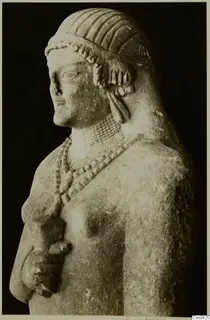 Limestone statue of a figure with ridged hair, a bead necklace and one arm bent at the waist