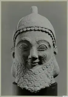 Limestone head of a bearded sculpture wearing a cap, on a dark cylindrical base