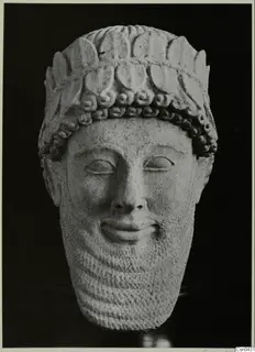 Limestone head of a bearded male figure with a curled hair band, photographed against a black background.