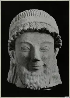 Limestone head of a bearded male sculpture with a wrapped headdress and carved curled hair and beard.
