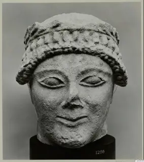 Limestone head of a figure with a banded headdress and almond-shaped eyes, shown on a black stand.
