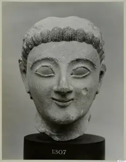 Limestone sculpted head of a figure with rows of curled hair and a faint smile, on a dark base.