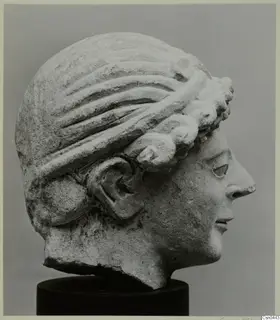 Limestone head of a female figure in profile, with wavy hair and a wreath-like band, on a black stand.