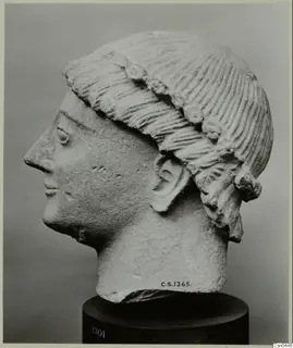 Limestone head of a figure in profile, with ridged hair bound by a band, on a dark stand.